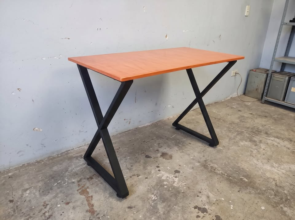 Vista completa del escritorio industrial con tablero de terciado y patas de acero en X dentro del taller